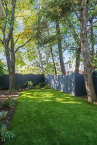 A well-maintained backyard with vibrant artificial grass and a variety of trees, offering a peaceful retreat.